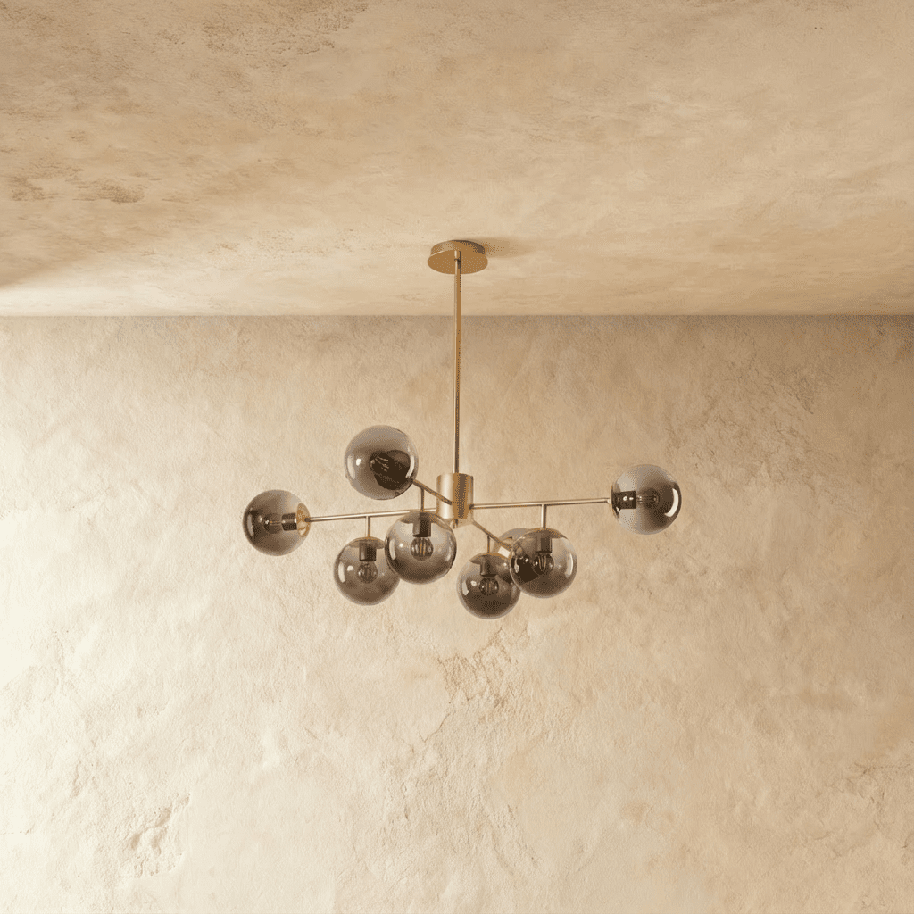 Clérachic gold chandelier with 7 smoky grey glass globes on straight arms, unlit, against a limewash wall.