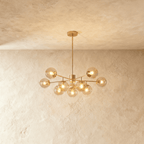 Clérachic gold chandelier with 9 cognac glass globes on straight arms, lit warm, against a limewash wall.