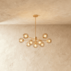 Clérachic gold chandelier with 9 smoked glass globes on straight arms, lit warm, against a limewash wall.