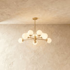 Clérachic gold chandelier with 9 milky white glass globes on straight arms, lit warm, against a limewash wall.