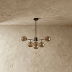 Clérachic black chandelier with 5 smoked glass globes on straight arms, unlit, against a limewash wall.