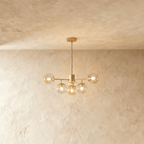 Clérachic gold chandelier with 5 cognac glass globes on straight arms, lit warm, against a limewash wall.