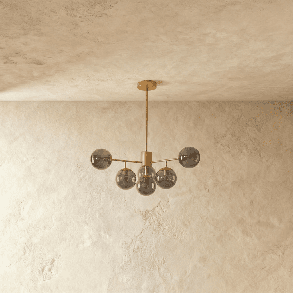 Clérachic gold chandelier with 5 smoky grey glass globes on straight arms, unlit, against a limewash wall.