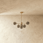Clérachic gold chandelier with 5 smoky grey glass globes on straight arms, unlit, against a limewash wall.