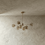 Clérachic gold chandelier with 7 cognac-tinted glass globes on straight arms, unlit, against a limewash wall.