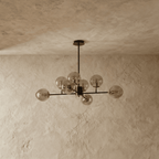 Clérachic black chandelier with 8 cognac-tinted glass globes on straight arms, unlit, against a limewash wall.