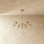 Clérachic silver chandelier with 9 clear glass globes on straight arms, unlit, against a limewash wall.