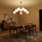 Clérachic gold chandelier with 9 milky white glass globes above a walnut dining table, glowing in the evening, in a warm room.