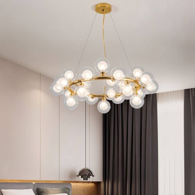 Clérachic gold ring chandelier of clear glass globes with frosted inner bulbs, hung on fine cables in a calm, neutral bedroom.