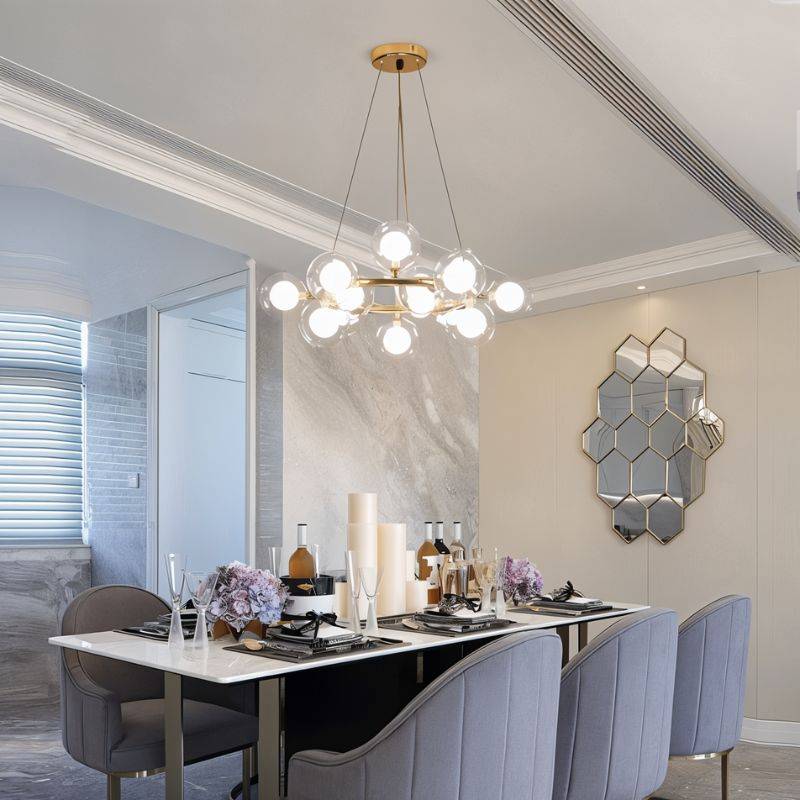 Clérachic compact gold ring chandelier of clear glass globes with glowing inner bulbs, hung over a marble-topped dining table.
