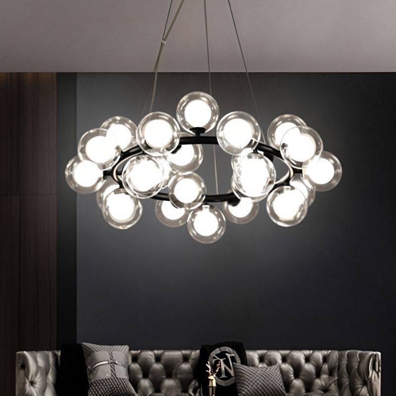 Clérachic black ring chandelier of clear glass globes with frosted inner bulbs, glowing above a tufted grey leather sofa.