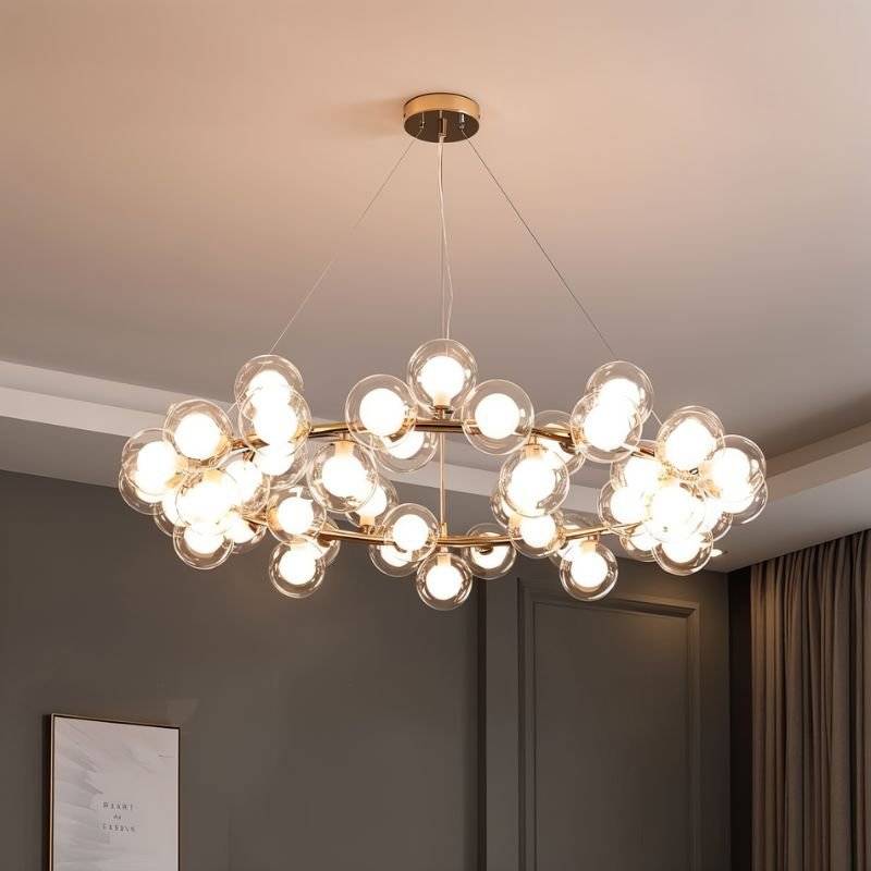 Clérachic large gold ring chandelier with clear glass globes and lit frosted bulbs, in a room with grey panelled walls.