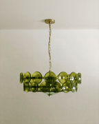 Clérachic two-tier chandelier with olive-green glass discs on a brass frame, hung on a fine brass chain against a pale ceiling.