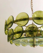 Clérachic chandelier close-up: round green glass discs on brass bars above a clear glass bowl with a bare filament bulb.