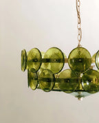 Clérachic chandelier seen from below, olive-green rippled glass discs fixed to brass bands with small pins and a glass base.