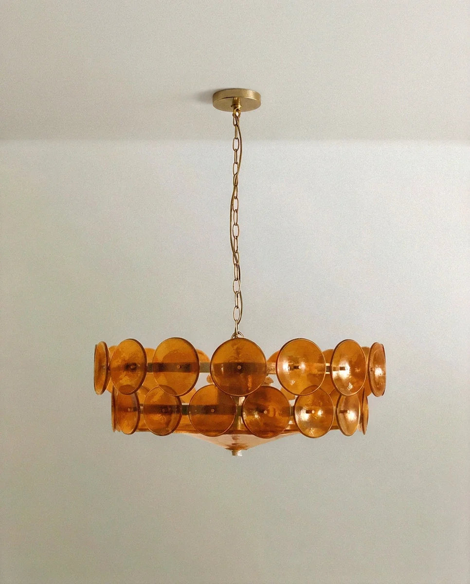 Clérachic two-tier chandelier with amber-orange glass discs on a brass frame, hanging from a brass chain and round canopy.