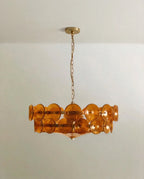 Clérachic two-tier chandelier with amber-orange glass discs on a brass frame, hanging from a brass chain and round canopy.