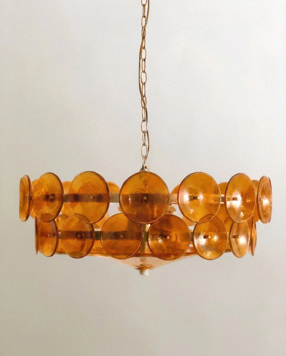 Clérachic chandelier hung low, tiers of amber glass discs on slim brass bars with a glass bowl and small white finial below.