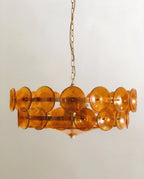 Clérachic chandelier hung low, tiers of amber glass discs on slim brass bars with a glass bowl and small white finial below.