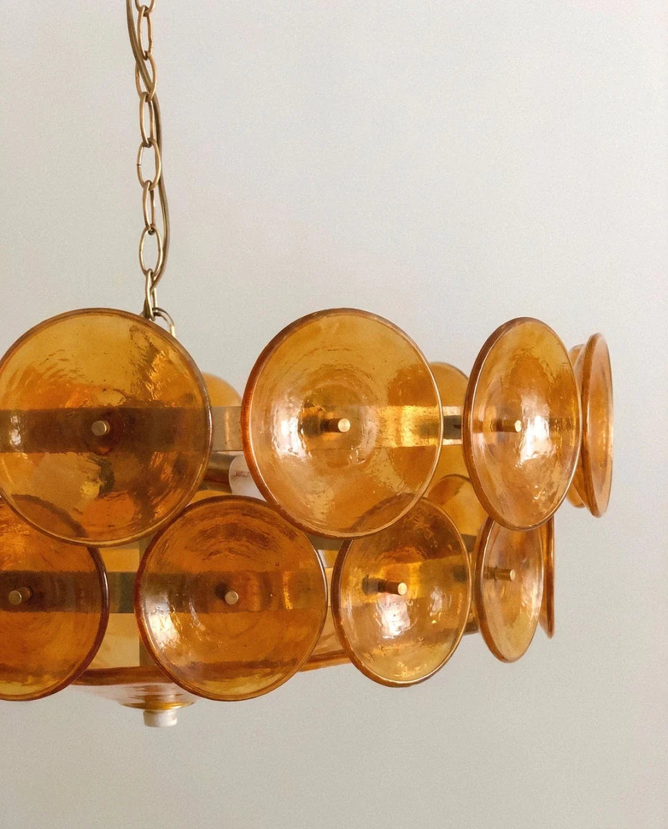 Clérachic chandelier close-up of amber glass discs with a hammered texture, each held on a brass pin and band.