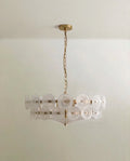 Clérachic chandelier with frosted, milky glass discs in two tiers on a brushed brass frame and chain, on a pale ceiling.