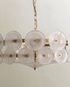 Clérachic chandelier close-up of milky frosted glass discs on brass pins, with a shallow glass bowl beneath the lower tier.