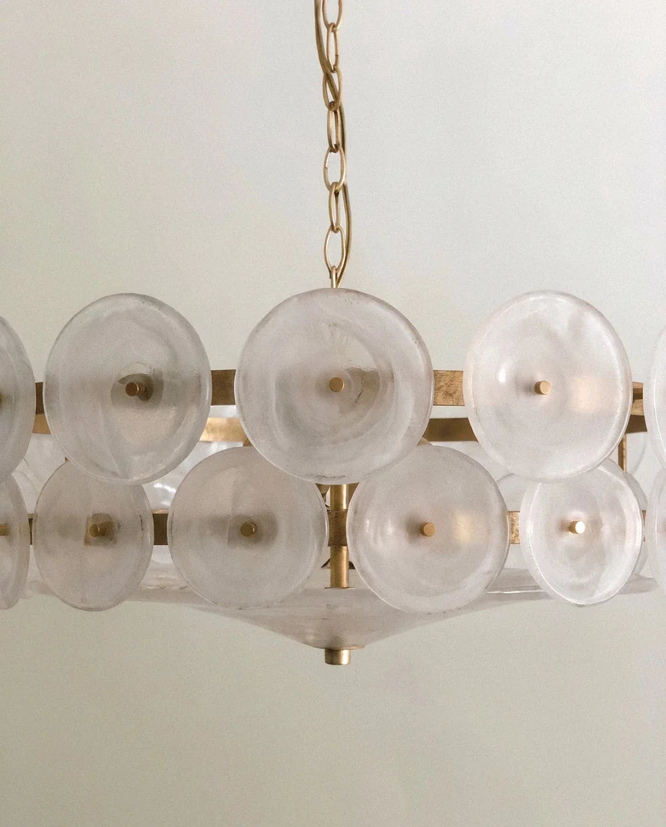 Clérachic chandelier close-up of milky frosted glass discs on brass pins, with a shallow glass bowl beneath the lower tier.