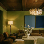 Clérachic disc chandelier lit in a living room with olive walls, a velvet sofa, a floor lamp and a vase of daisies.