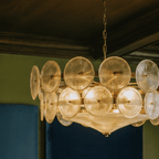 Clérachic chandelier glowing warm, its textured champagne glass discs and brass arms close up against a dark wood ceiling.