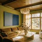 Clérachic disc chandelier hung over a sunlit sitting room with a velvet sofa, blue wall panels and a travertine coffee table.