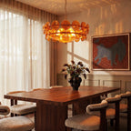 Clérachic chandelier with lit amber glass discs above a walnut dining table, with sheer curtains and wall art behind it.
