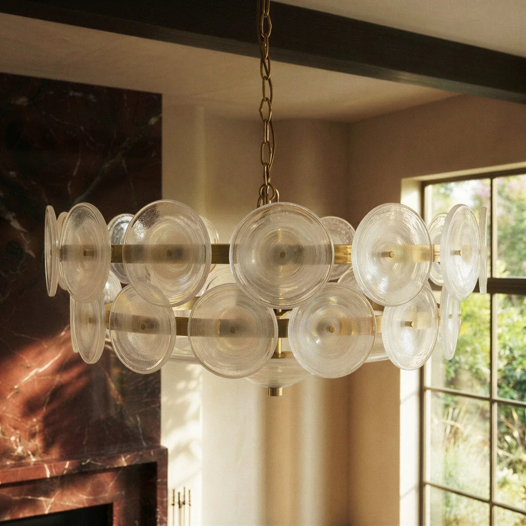 Clérachic chandelier close-up of clear ribbed glass discs on brass bands, in a room with a dark marble fireplace and window.