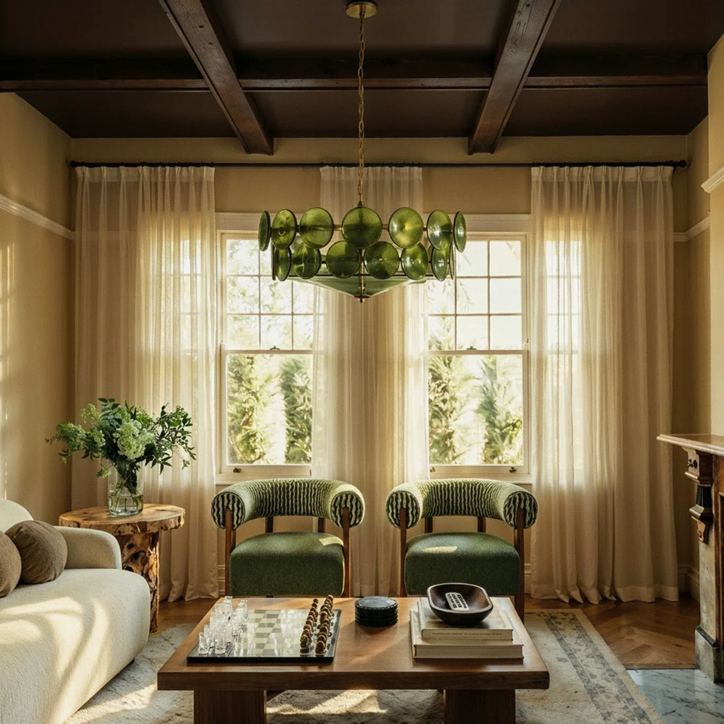 Clérachic chandelier with green glass discs and brass chain under dark beams, above a coffee table between two green armchairs.