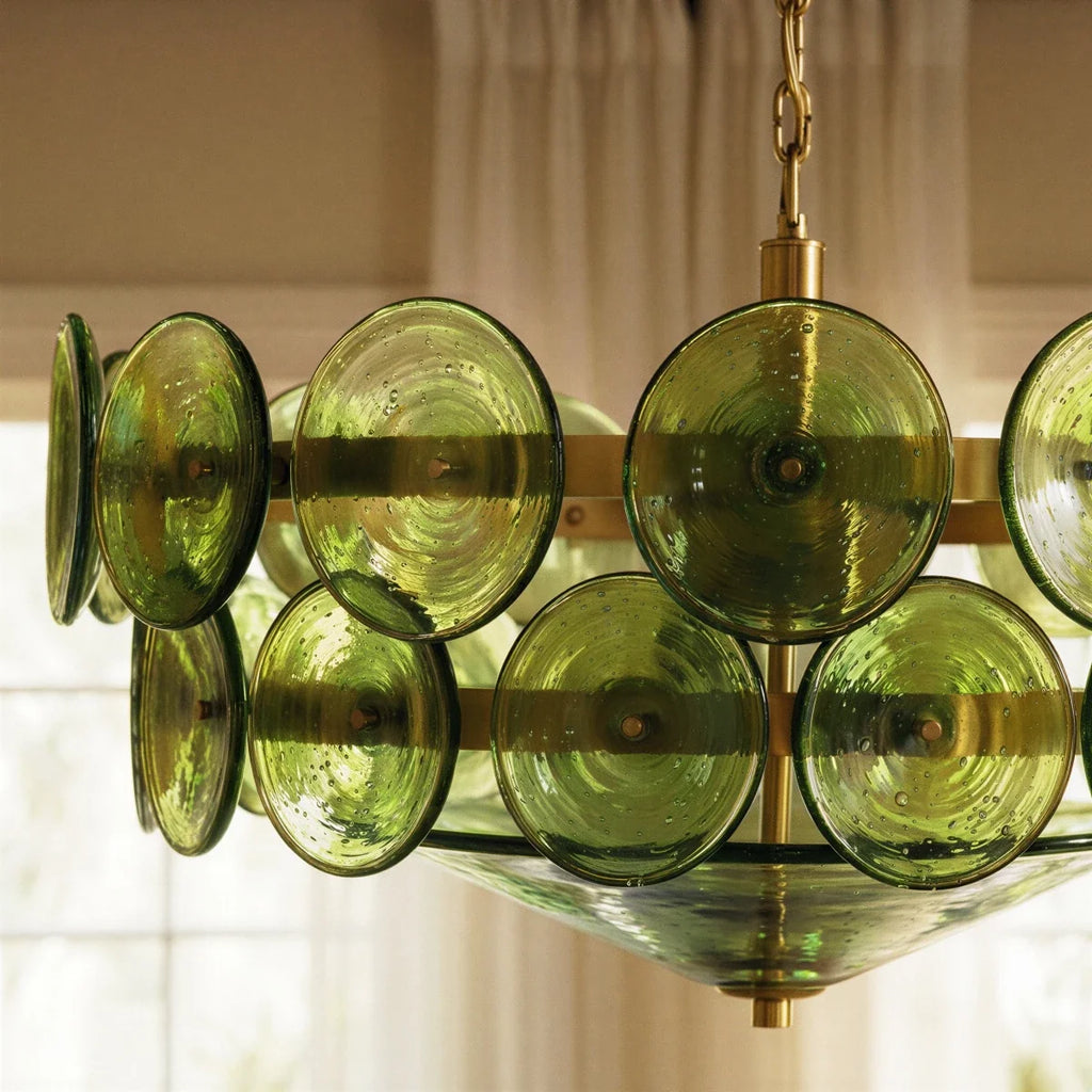 Clérachic chandelier close-up of bubbled green glass discs on brass bands, with a glass cone beneath and sheer curtains behind.