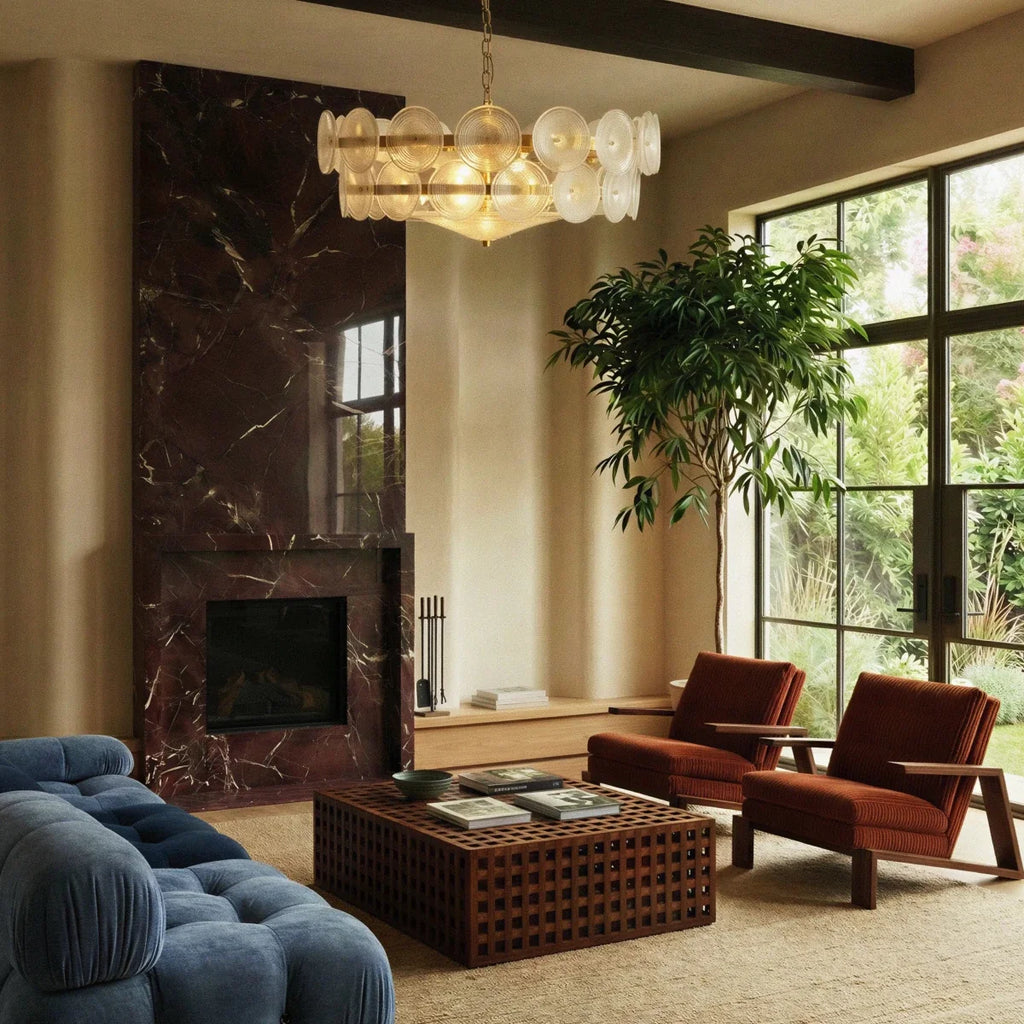 Clérachic disc chandelier lit warm in a living room with a dark marble fireplace, a tall plant and rust-coloured armchairs.