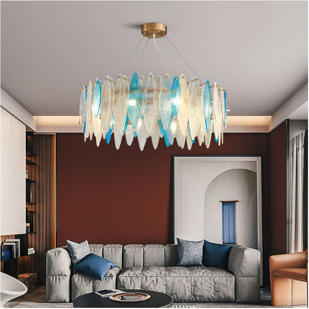 Clérachic glass chandelier with clear and blue leaf panels over a grey sofa, in front of a rust-red wall.