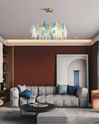 Small Clérachic chandelier with blue and clear glass leaves above a grey sofa and round coffee table.