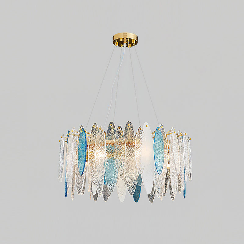 Clérachic chandelier with clear and blue glass leaves on a gold frame, lit and hanging on a grey backdrop.