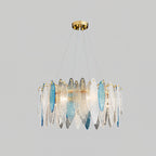 Clérachic chandelier with clear and blue glass leaves on a gold frame, lit and hanging on a grey backdrop.