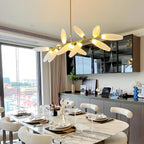 A Clérachic chandelier with warm-lit frosted glass leaves hangs over a marble dining table laid for dinner, with city views through the window.