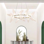 A round Clérachic chandelier of frosted white leaves on a gold ring hangs in a bright entrance with an arched mirror and a green-framed doorway.