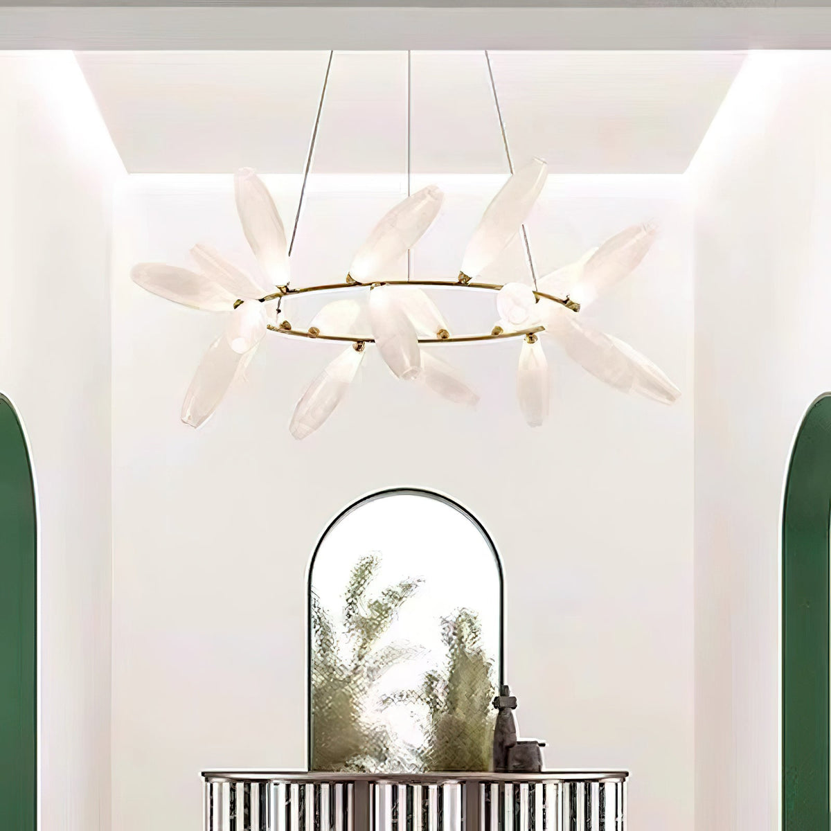 A round Clérachic chandelier of frosted white leaves on a gold ring hangs in a bright entrance with an arched mirror and a green-framed doorway.