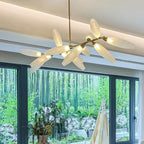 A Clérachic chandelier glows warm beneath a coved ceiling, its glass leaves branching on a gold rod in front of a window onto a garden of trees.