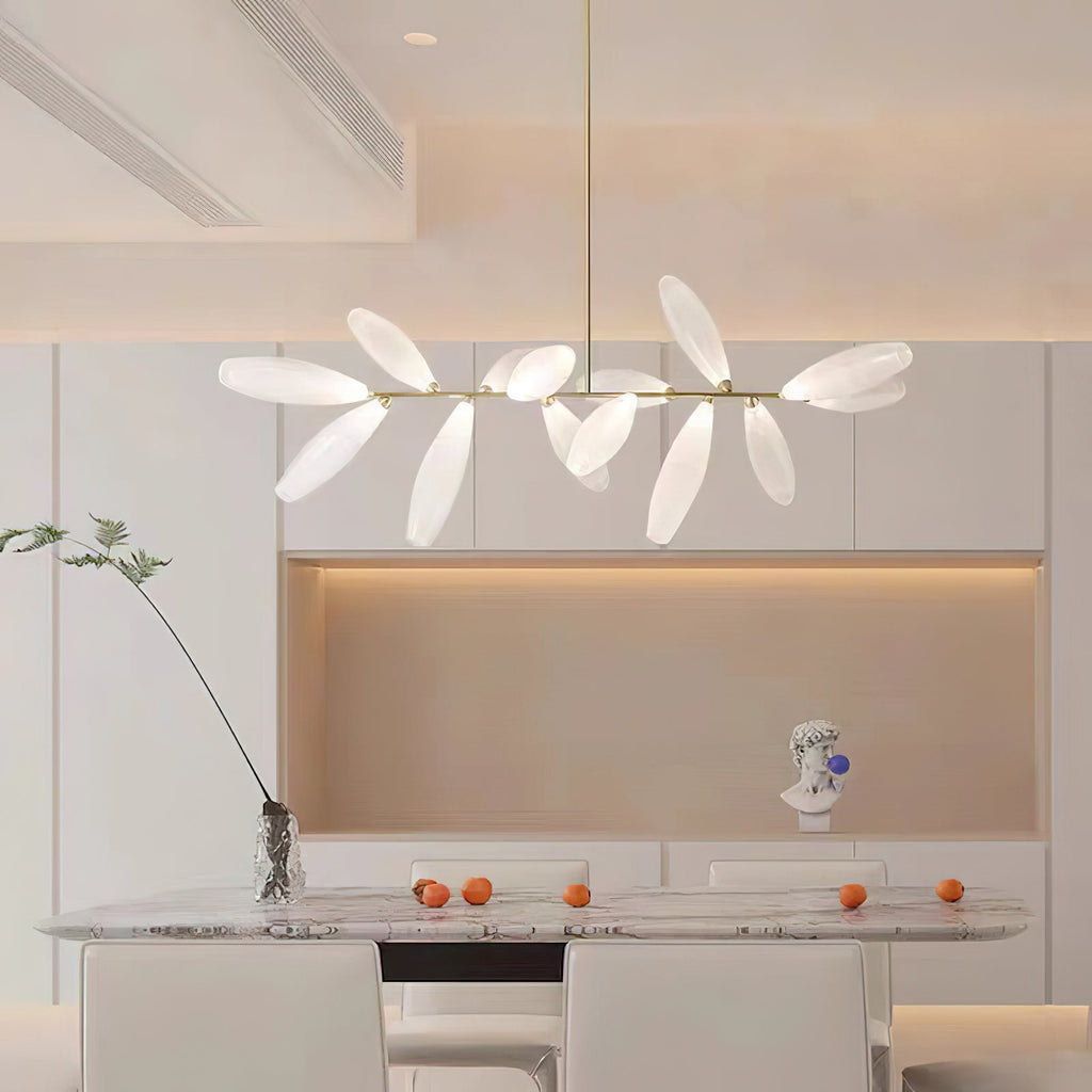 A linear Clérachic chandelier of frosted leaves hangs above a marble table with a few oranges and a slim stem in a pale, minimal dining room.
