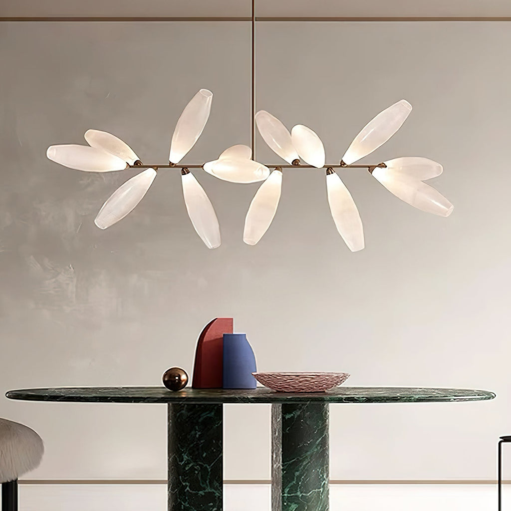 A linear Clérachic chandelier of frosted glass leaves on a gold bar hangs above a dark green marble table and a pink dish.