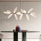 A linear Clérachic chandelier of frosted glass leaves on a gold bar hangs above a dark green marble table and a pink dish.