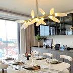 A Clérachic chandelier glows warm above a marble dining table set for a meal, with a glazed cabinet and a tall window behind.