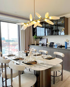 A wider view of a Clérachic chandelier lit warm above a marble dining table and cream bouclé chairs, with a glazed cabinet and a city view.