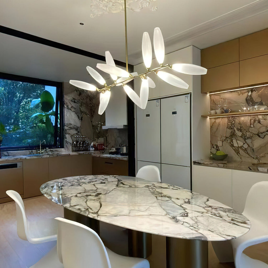 A Clérachic chandelier of lit white glass leaves hangs above a veined marble oval table in a kitchen with warm wood cabinets and white chairs.