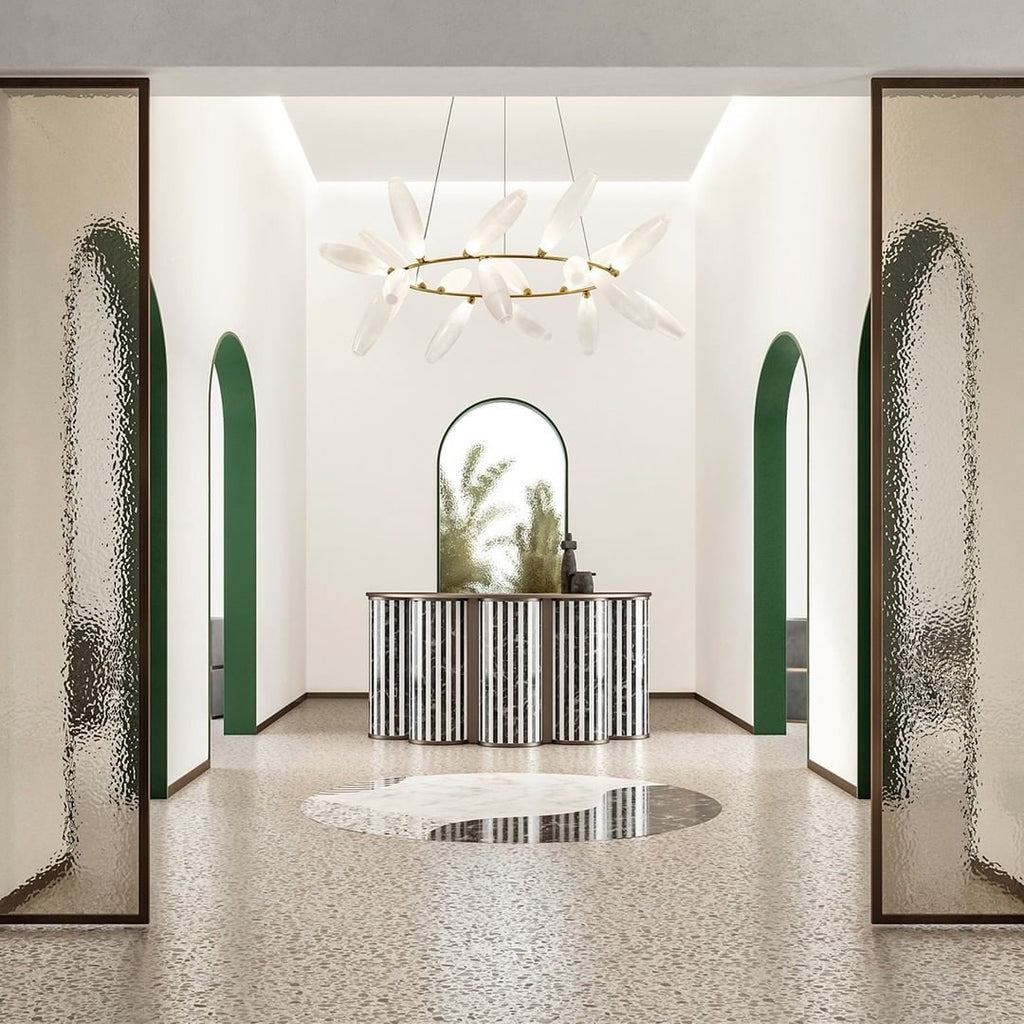 A round Clérachic chandelier on a gold ring hangs in a tall white entrance hall with green arches and patterned glass panels.